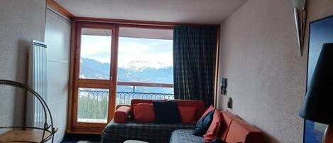 A compact room with a bed, a small table, and a window with a mountain view.