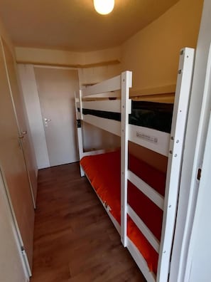 Una habitación pequeña con una cama litera de madera, una puerta y suelo de madera.
