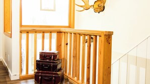 A staircase with wooden railings, a wall-mounted deer head decoration, and a stack of vintage suitcases at the bottom. - Kings Den resort (Revelstoke)