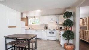 A modern kitchen with white cabinets, a wooden dining table, and a potted plant. - Kings Den resort (Revelstoke)
