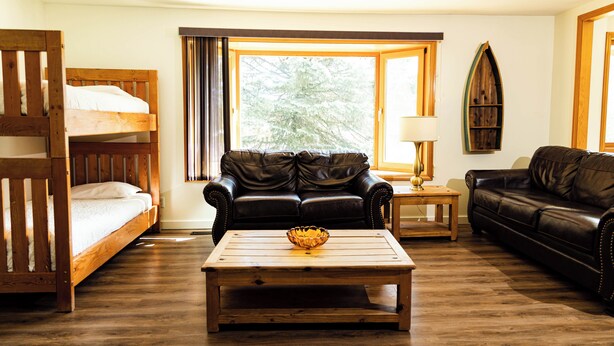 A room with a bunk bed, two leather sofas, a wooden coffee table, and a window with curtains. - Kings Den resort (Revelstoke)