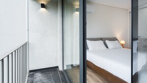 A modern hotel room with a bed, a nightstand with a lamp, and a view through a glass door.