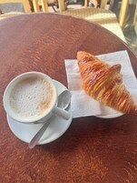 Una taza de café y un croissant sobre una mesa redonda.