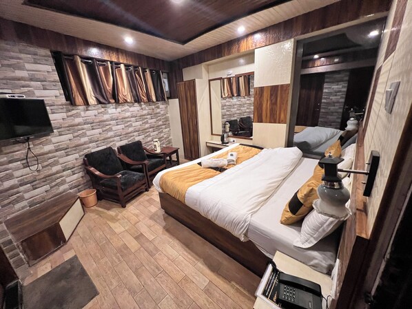 A modern hotel room with a stone wall, a bed with white linens, a wooden desk, a chair, a TV mounted on the wall, and a mirror. - Hotel Victory (Shimla)