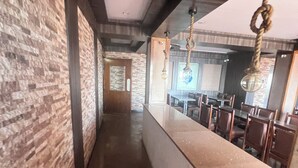 Un couloir avec un mur de briques d’un côté et un espace bar de l’autre. L’espace bar est équipé de chaises et de tables.