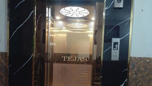 Un ascensor con una pantalla digital que muestra “0” y el mensaje “BIENVENIDO”, rodeado de paredes de mármol negro con vetas blancas.