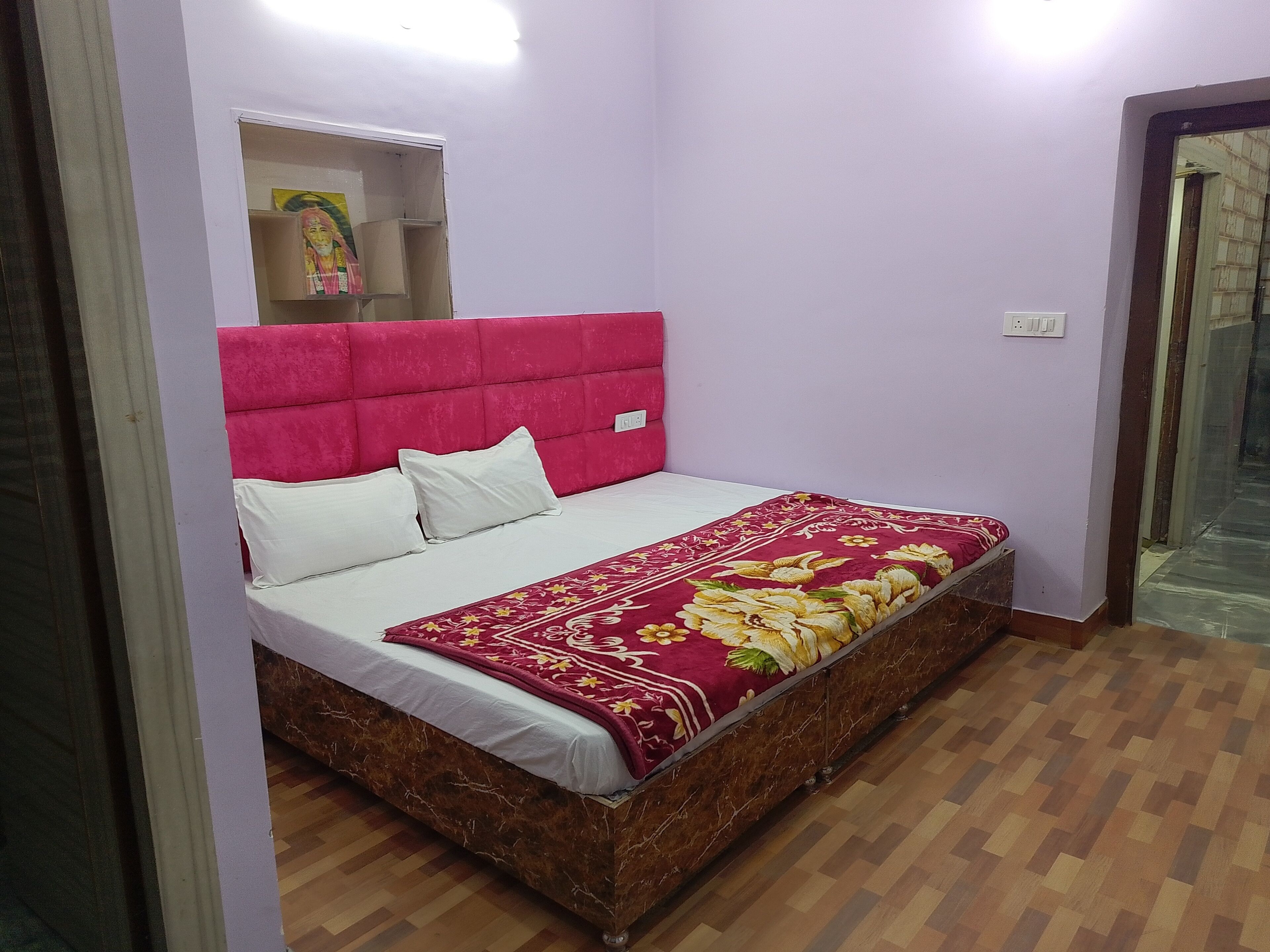 Ein Schlafzimmer mit einem Bett, einem pinkfarbenen Kopfteil, einer blumigen Tagesdecke und Holzboden.