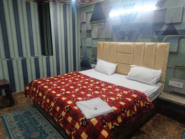 A hotel room with a bed, a headboard, a nightstand, a desk, and a window. - Tejas Dream House (Amritsar)