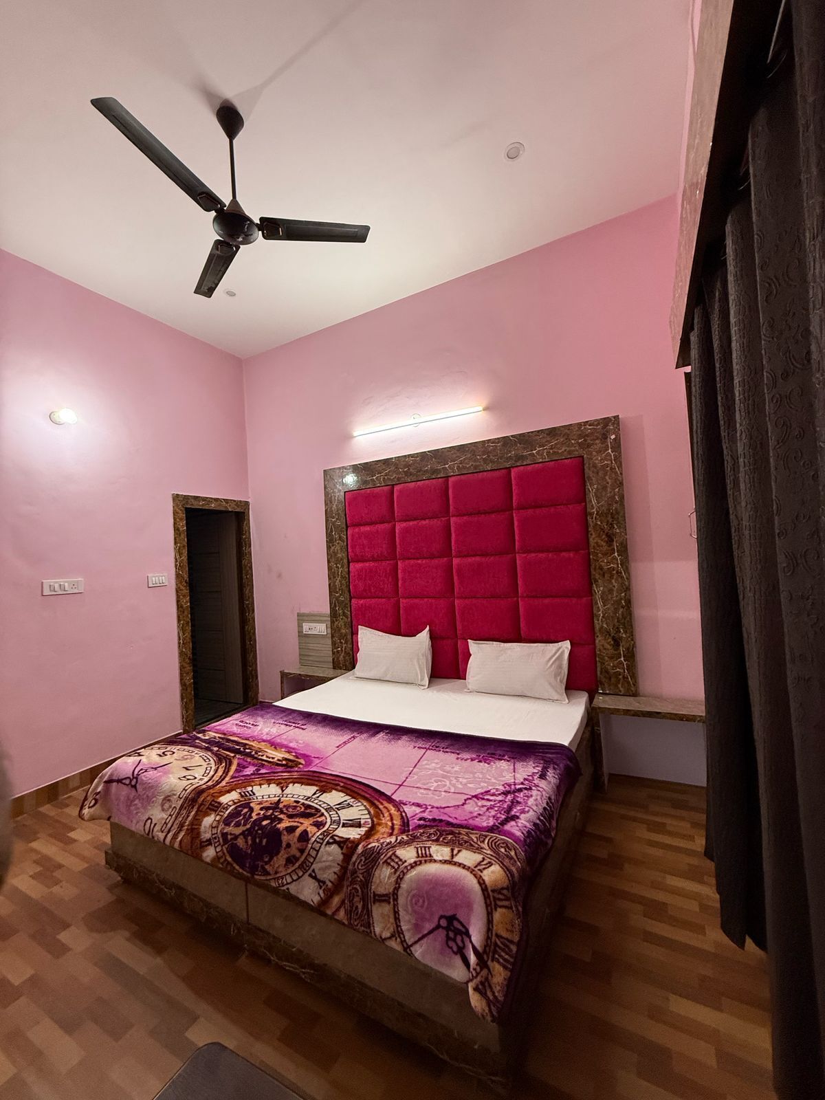 A bedroom with a bed, a ceiling fan, a headboard, and a wall-mounted light.