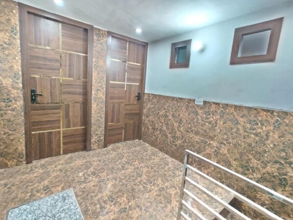 A room with two wooden doors, a marble floor, a small window, and a metal railing.