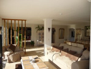Relax in a spacious living area with a sofa set, coffee table, and dining table, surrounded by lush greenery.
