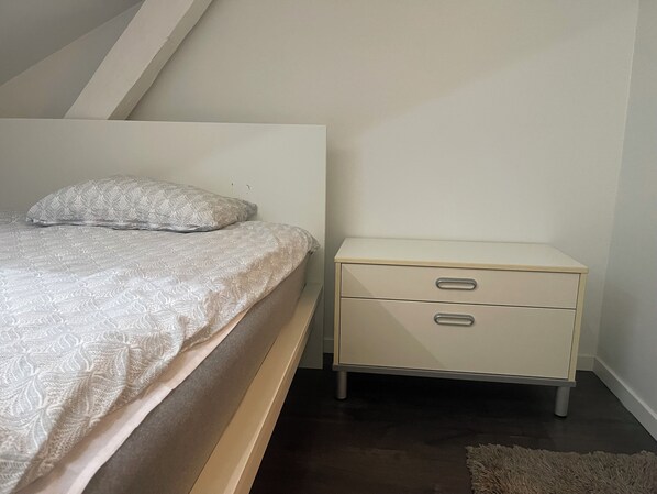 A bedroom with a bed, a nightstand with drawers, and a carpeted floor.