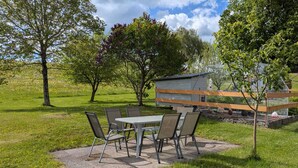 Un patio con mesa y sillas, rodeado de árboles y una zona delimitada por una valla.