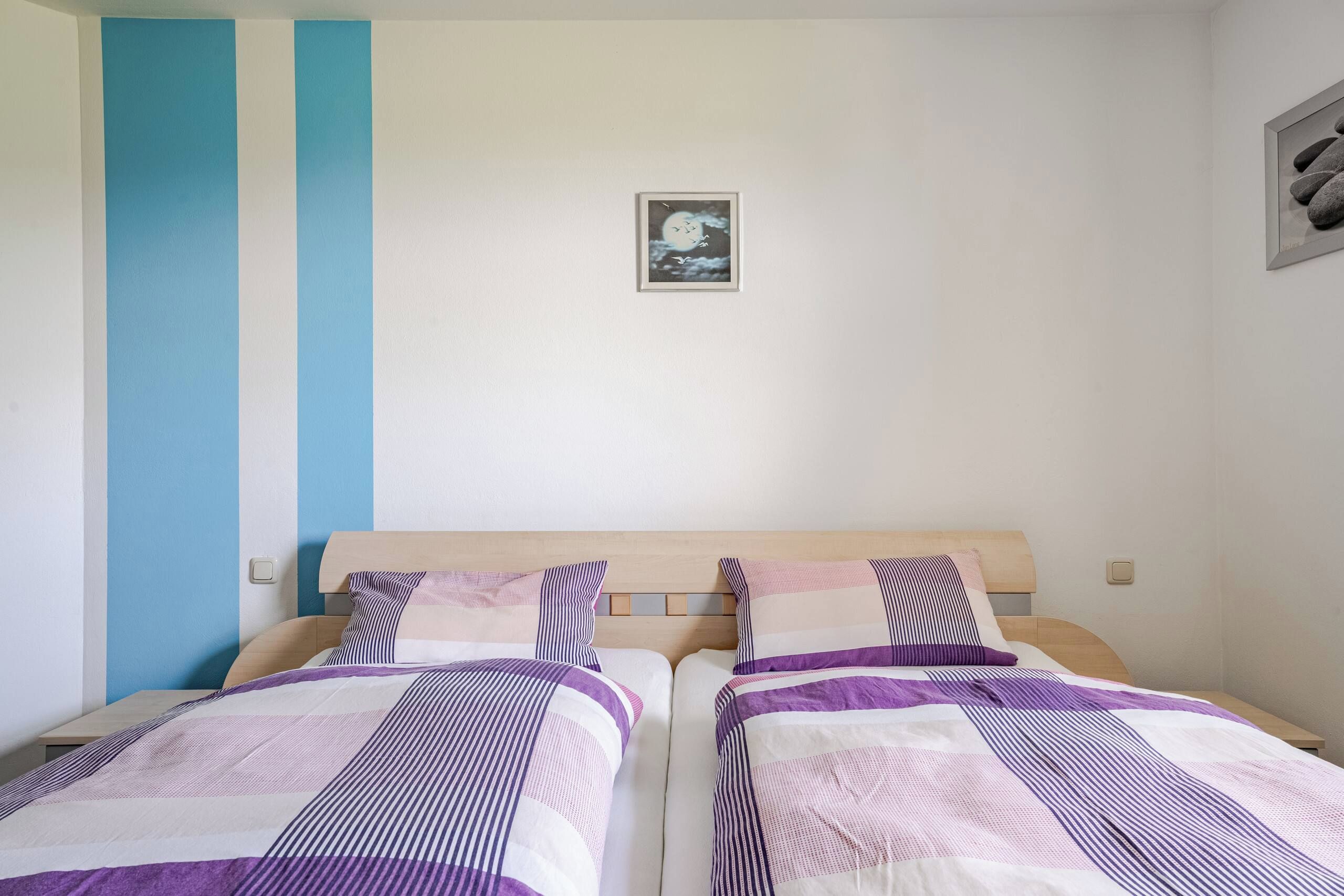 Un dormitorio con dos camas, pared azul, un cuadro enmarcado y una pared de piedra.