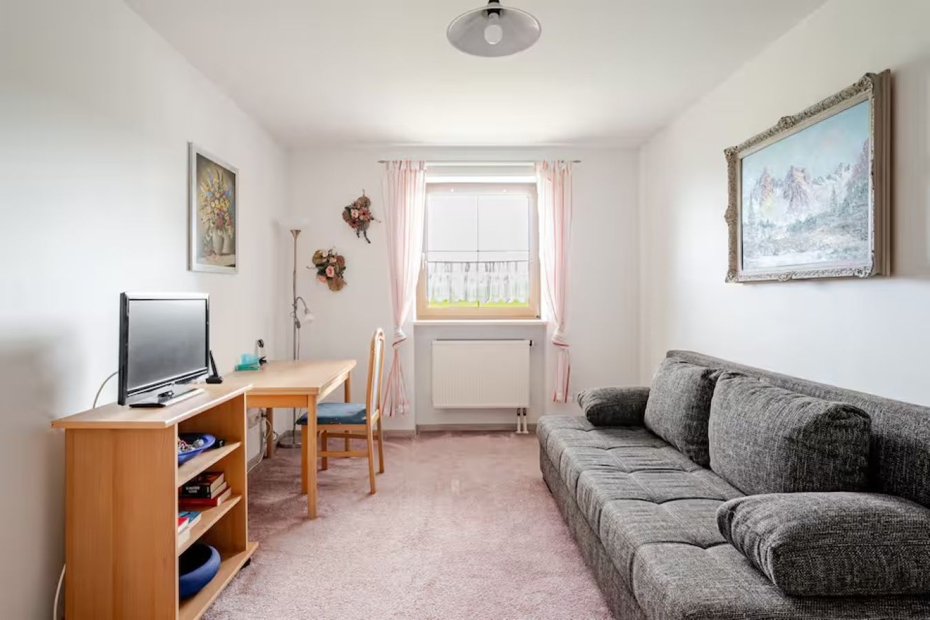 Een woonkamer met een grijze bank, een houten tafel met een televisie, en een raam met gordijnen.