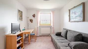 Een woonkamer met een grijze bank, een houten tafel met een televisie, en een raam met gordijnen.