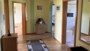 Un pasillo con pisos de madera, un tapete, un mueble con un jarrón y puertas que dan a otras habitaciones.