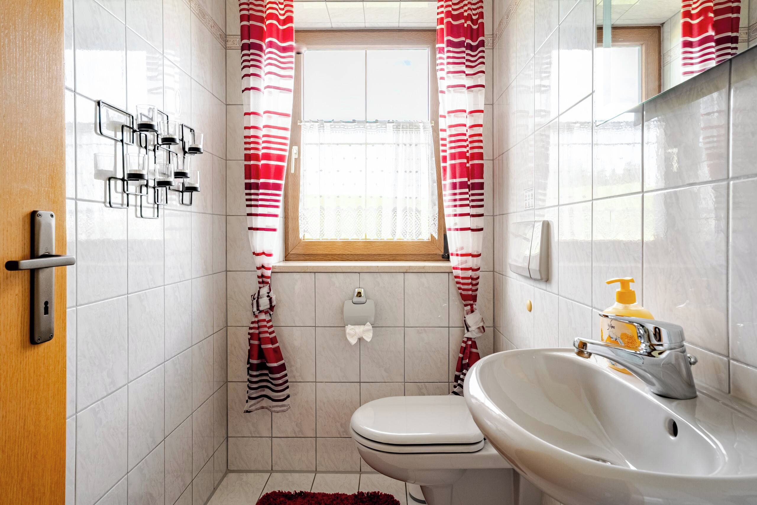 Et badeværelse med toilet, håndvask og et vindue med stribede gardiner.