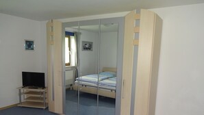 Un dormitorio con cama, televisor sobre un mueble, armario y ventana con cortinas.