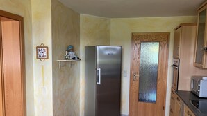 Una cocina con un refrigerador de acero inoxidable, armarios de madera, una silla de madera y un estante pequeño con un objeto decorativo.