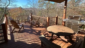 A wooden deck with Adirondack chairs, a table, and a grill.