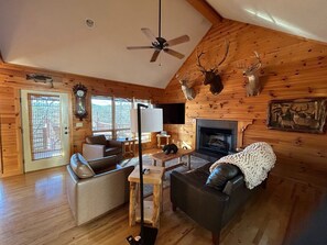 Un intérieur de chalet chaleureux avec une cheminée, des murs en bois, un ventilateur de plafond et des décorations en forme de bois de cerf.