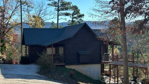 A rustic cabin with a sloped roof, a porch with a railing, and a deck with outdoor seating.