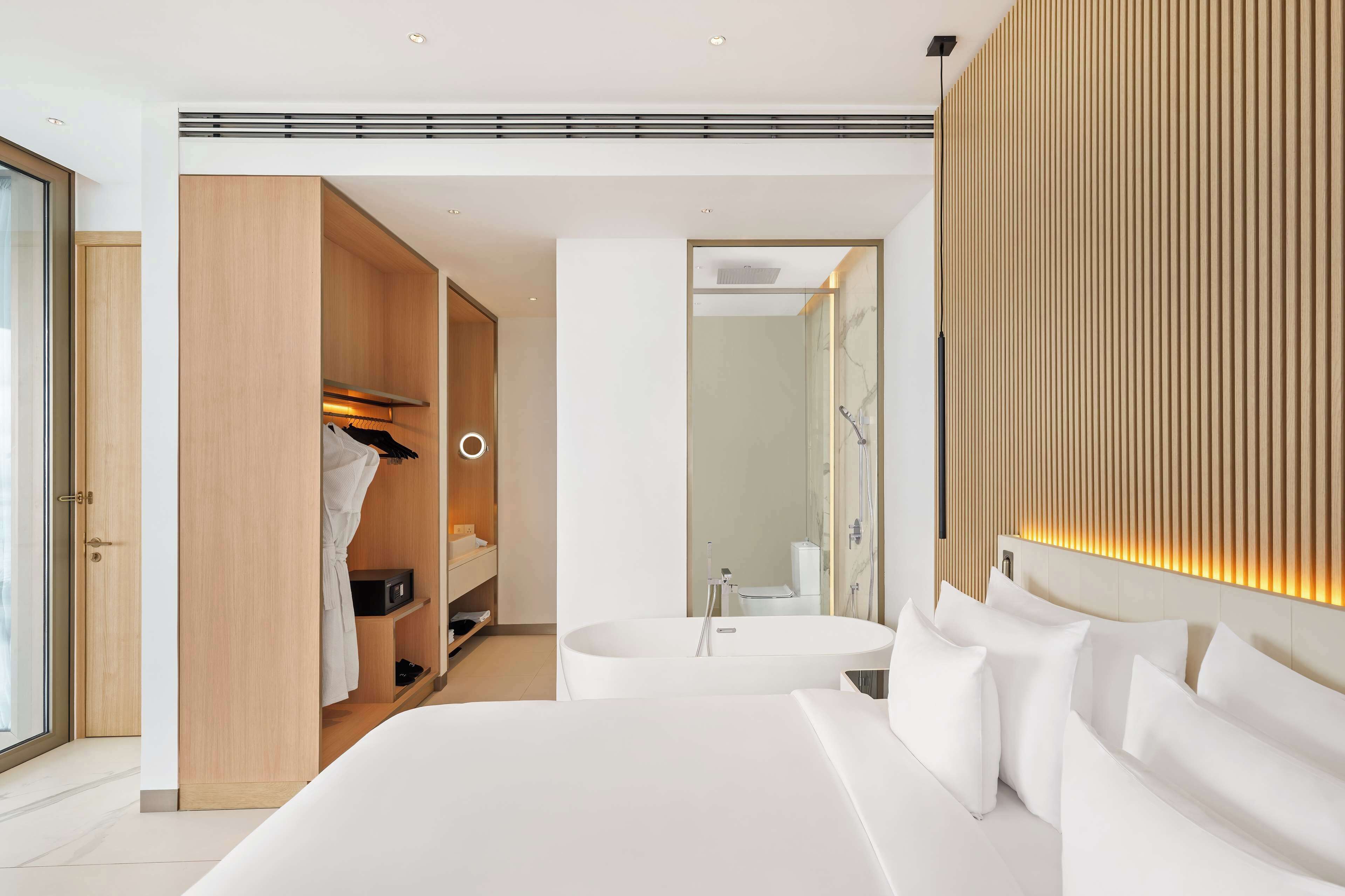 A modern bedroom with a large bed, a walk-in closet, a bathtub, and a shower.