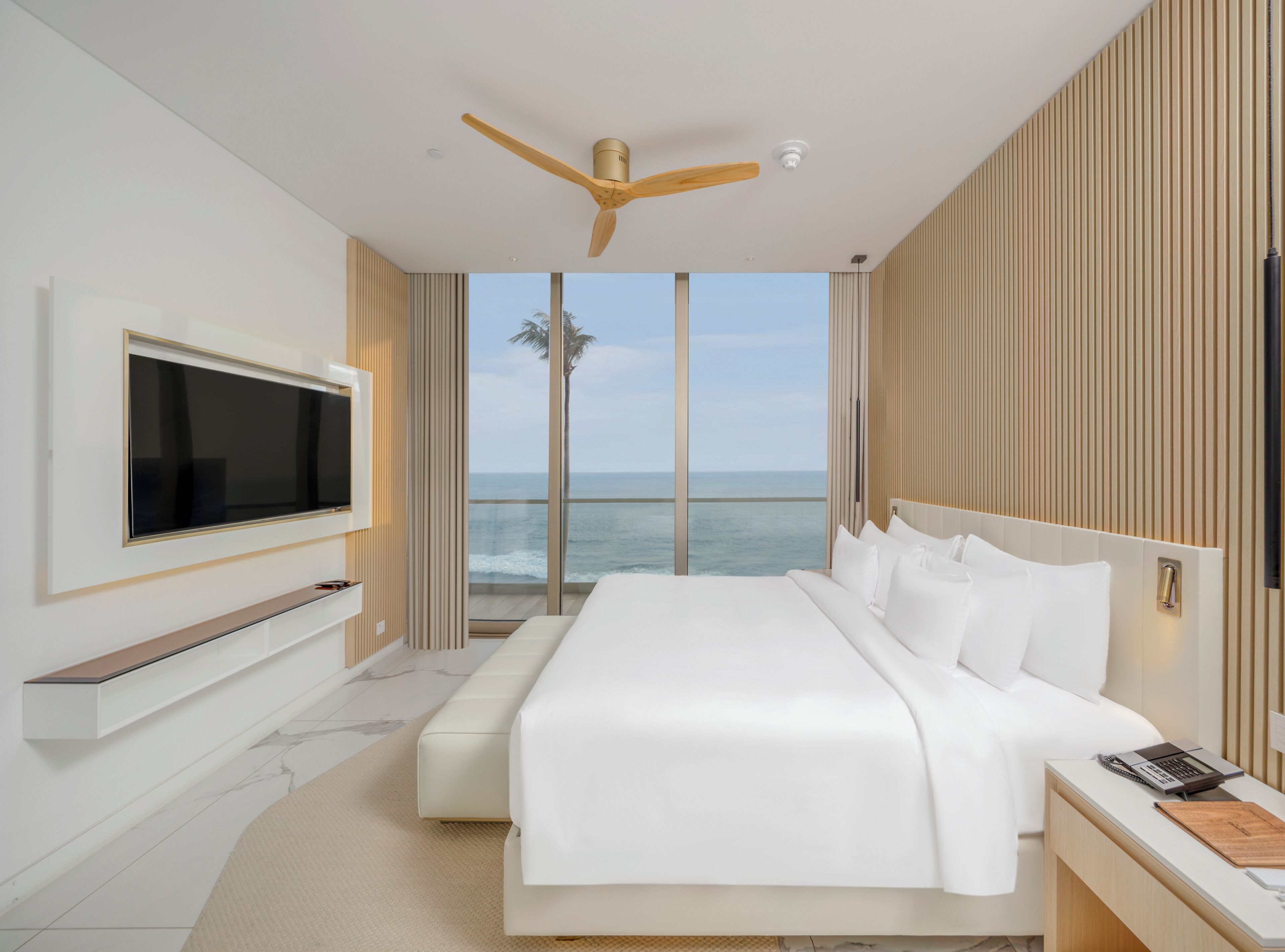 Een moderne hotelkamer met een groot bed, een flatscreen televisie aan de muur en uitzicht op de oceaan.