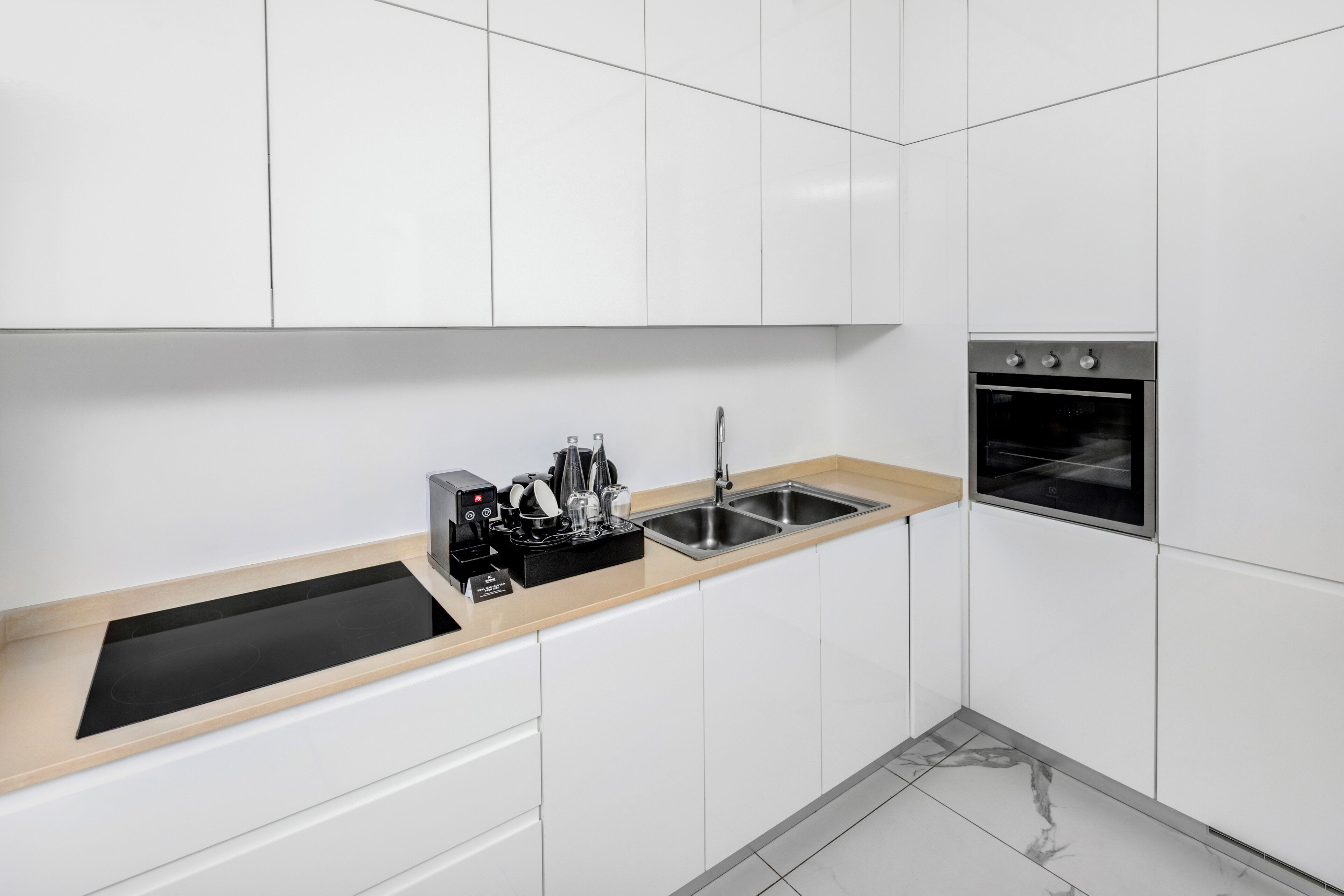 A modern kitchen with white cabinets, a black countertop, a stainless steel sink, and an oven.