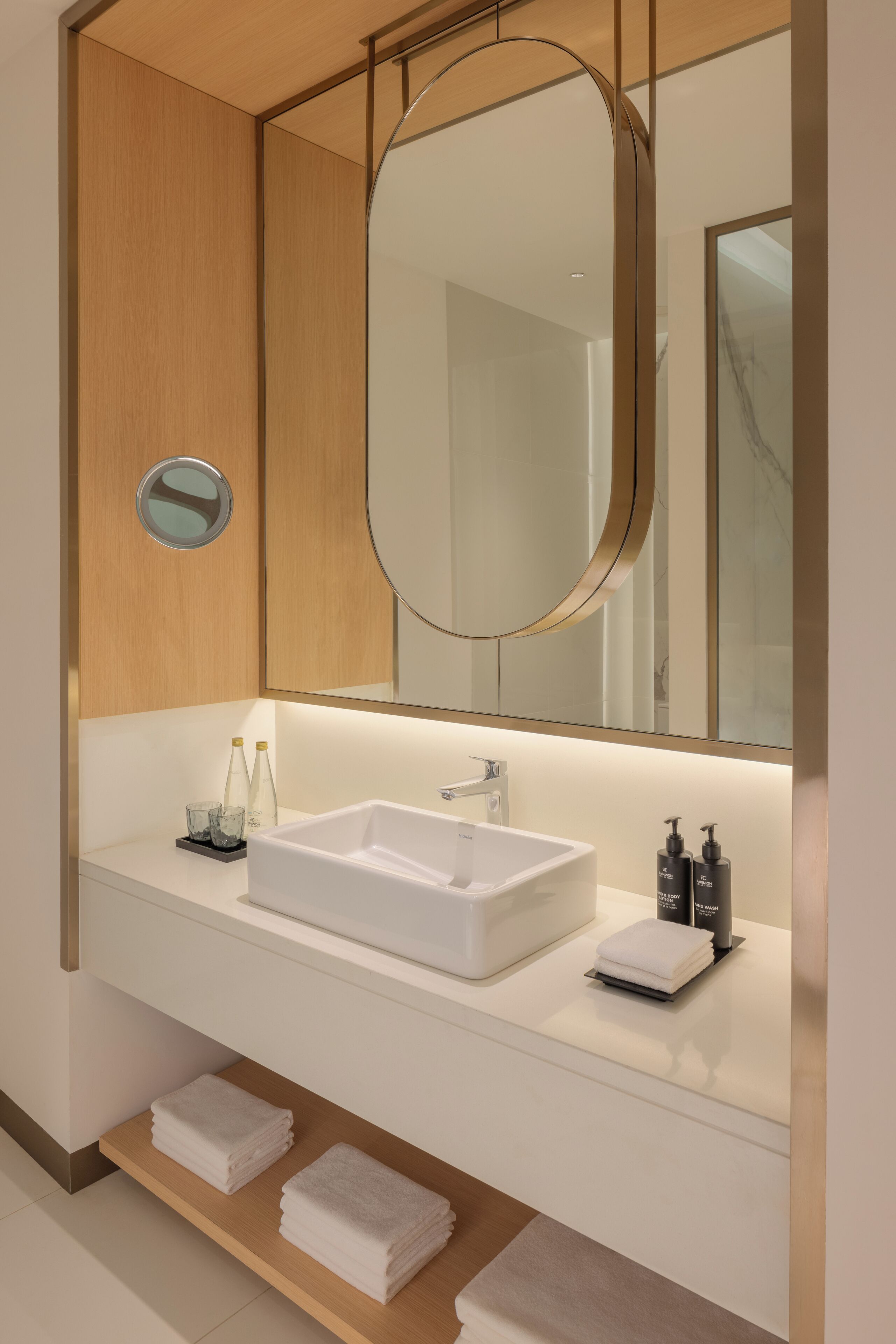 A modern bathroom with a white sink, a large mirror, and neatly folded towels on a shelf.
