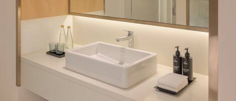 A modern bathroom with a white sink, a large mirror, and neatly folded towels on a shelf.