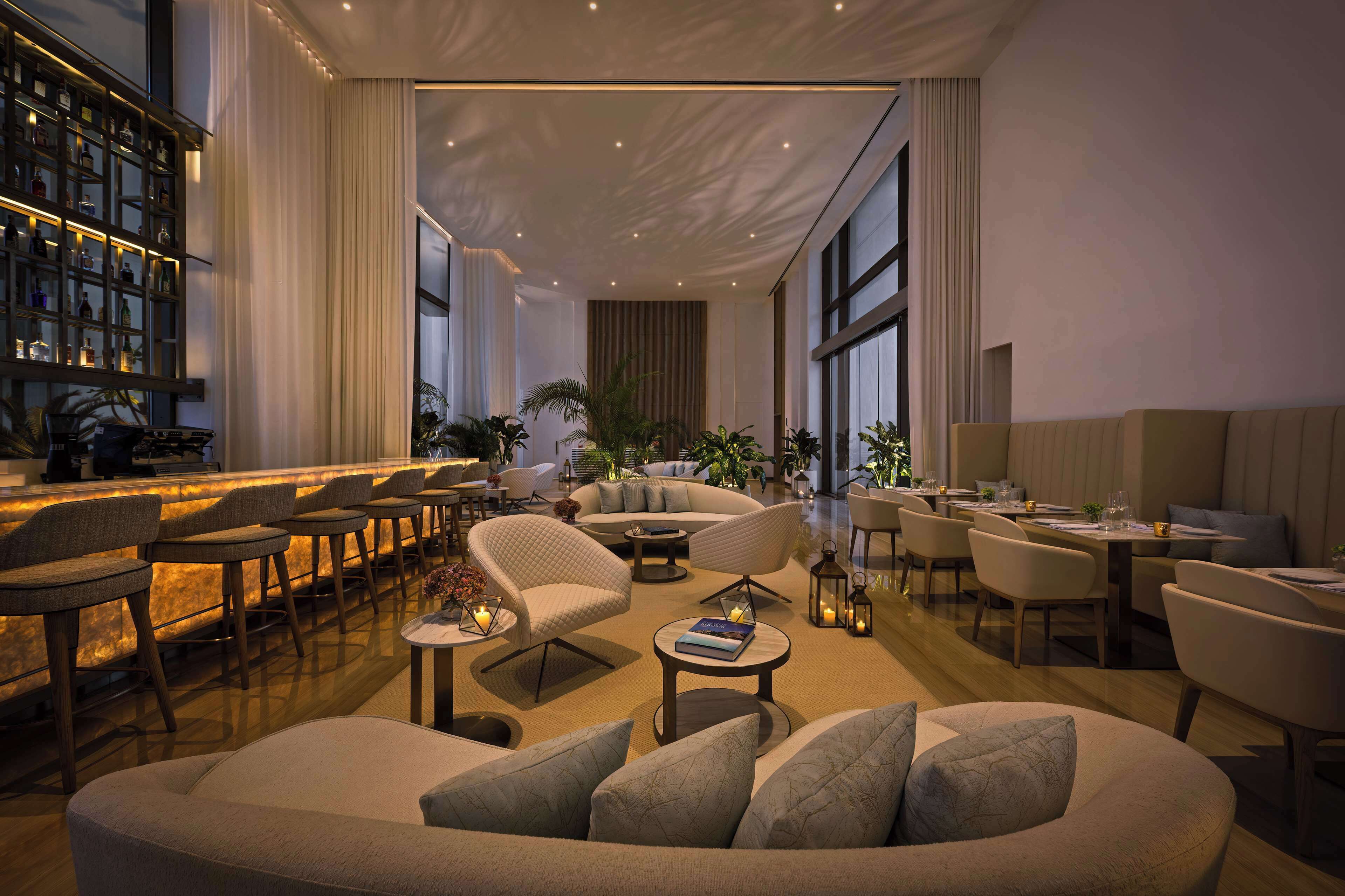 Una moderna hall d'albergo con zona bar, posti a sedere e ampie finestre.