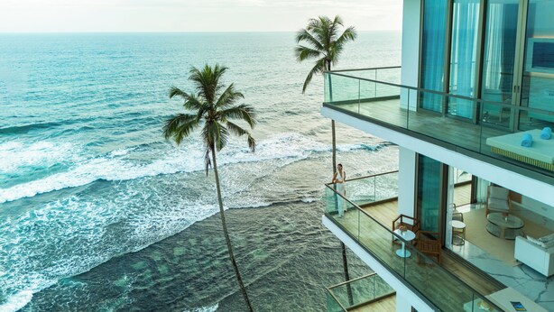 Un edificio moderno con balcón que da al océano, con barandilla de cristal y vista al mar.