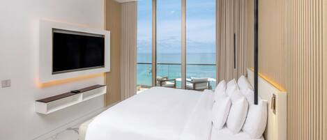 Een moderne hotelkamer met een groot bed, een aan de muur bevestigde televisie en een balkon met uitzicht op de oceaan.