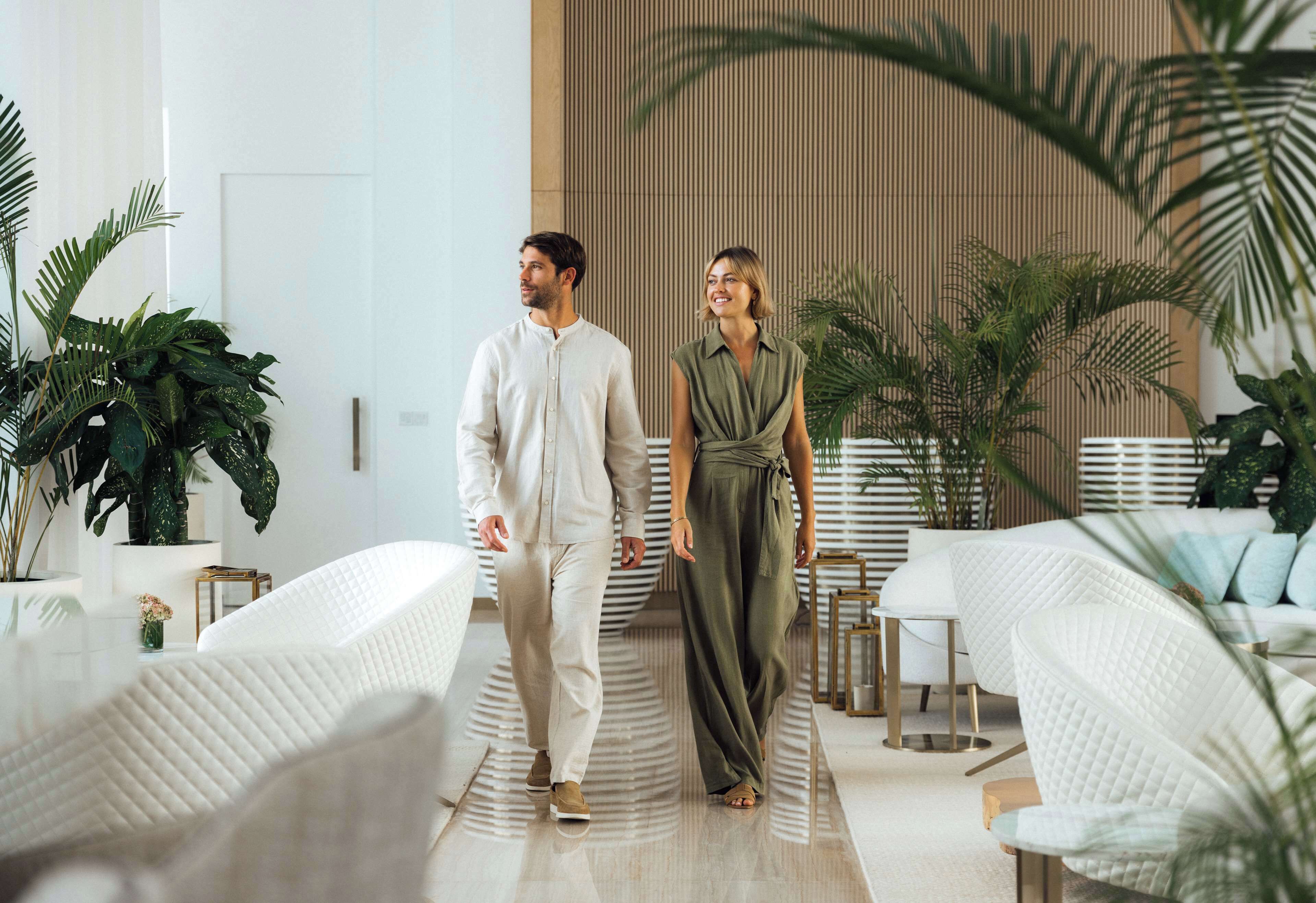 A modern hotel lobby with white furniture, potted plants, and a wooden accent wall.