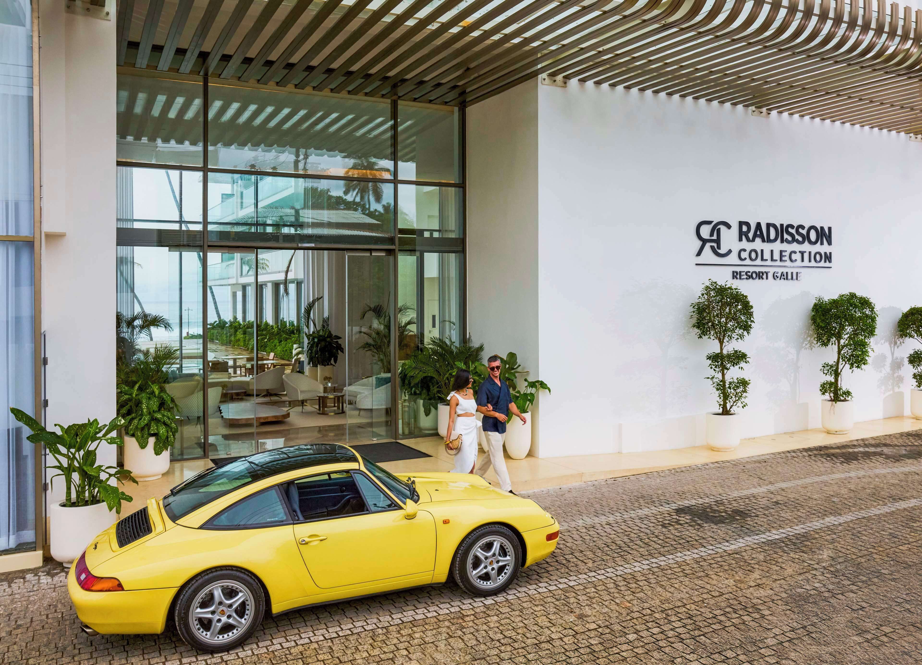 A modern building with a glass facade, a yellow sports car parked in front, and a sign reading "Radisson Collection Resort Galle".