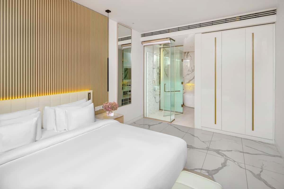 Une chambre d’hôtel moderne dotée d’un grand lit, d’un dressing et d’une douche à parois de verre.