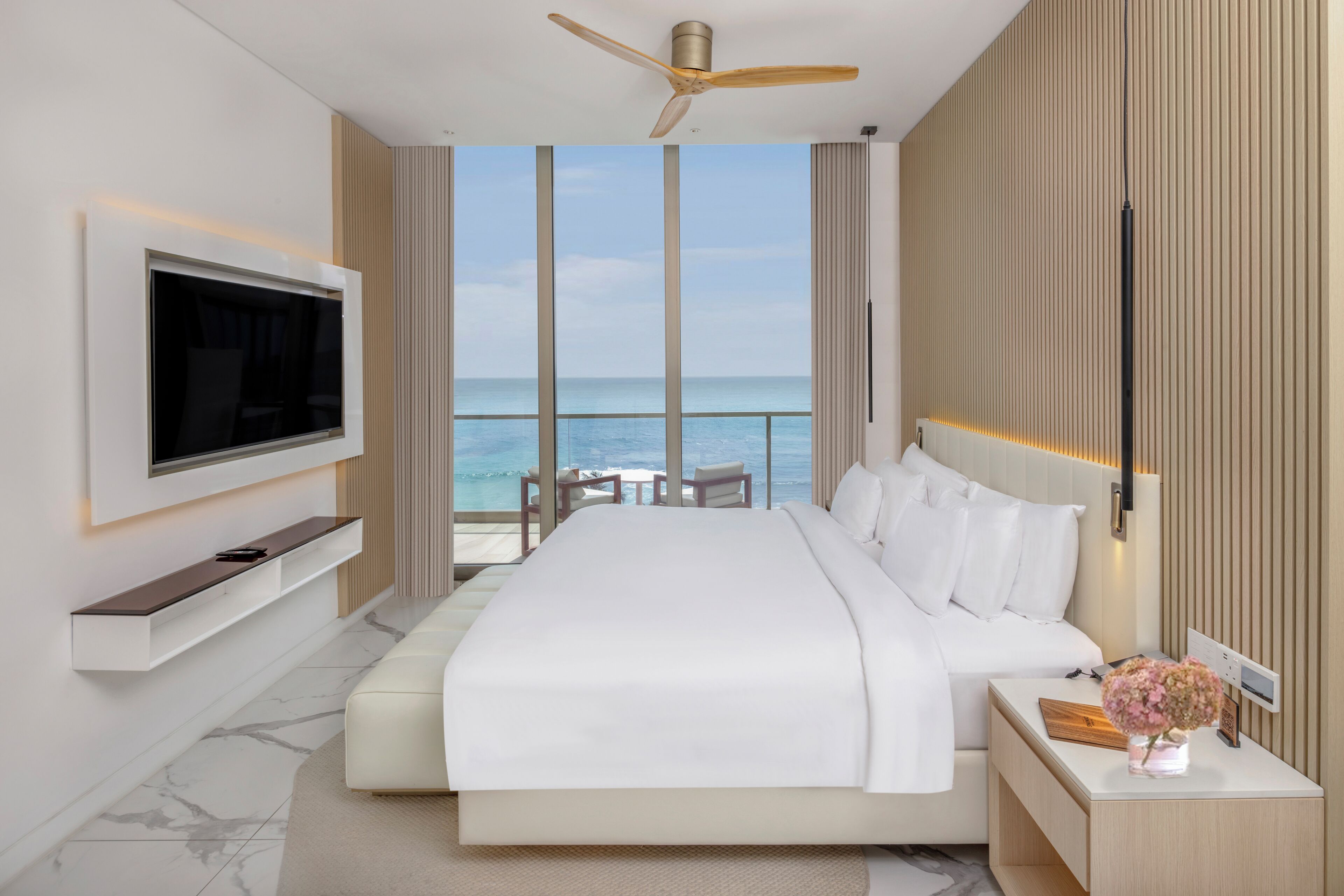 Un hotel moderno con una cama grande, un televisor de pantalla plana en la pared, una mesita con sillas y vistas al océano.