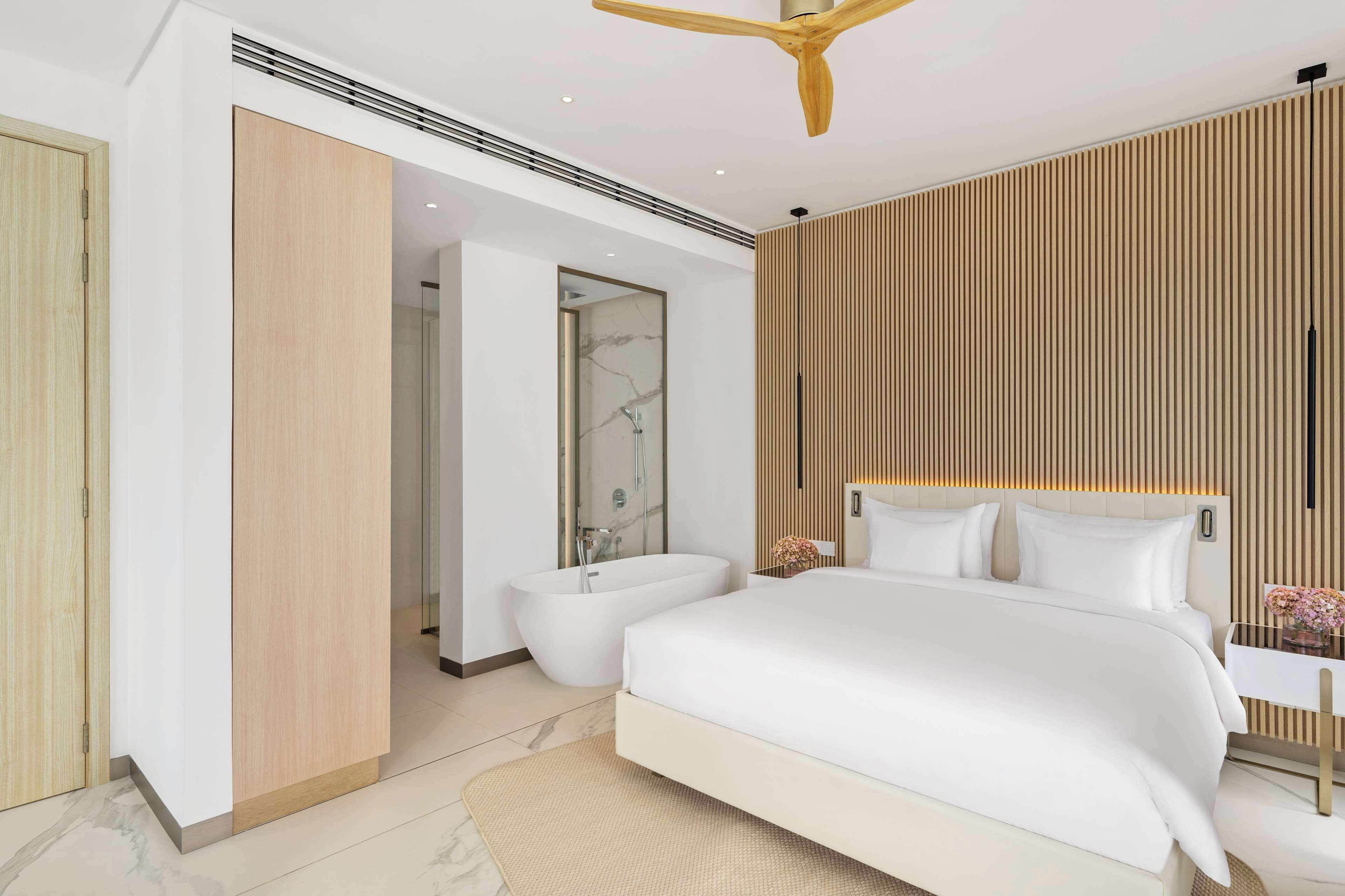 Ein modernes Schlafzimmer mit großem Bett, begehbarer Garderobe, freistehender Badewanne und Wandverkleidung aus Holz.