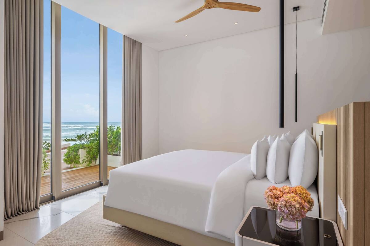 Une chambre d’hôtel moderne avec un grand lit, une vue sur l’océan et un ventilateur de plafond.