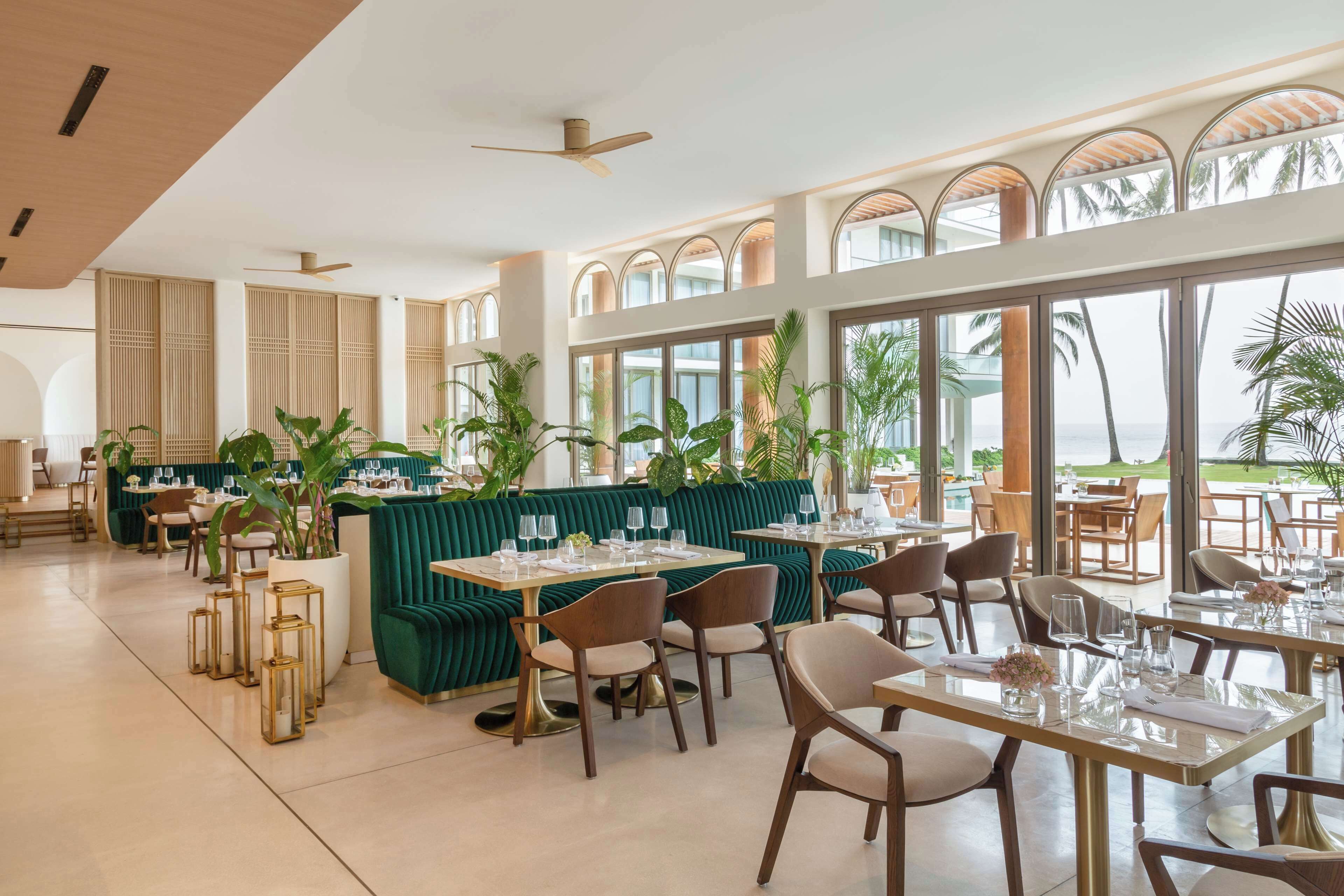 A spacious restaurant with high ceilings, large windows, and a view of the ocean.