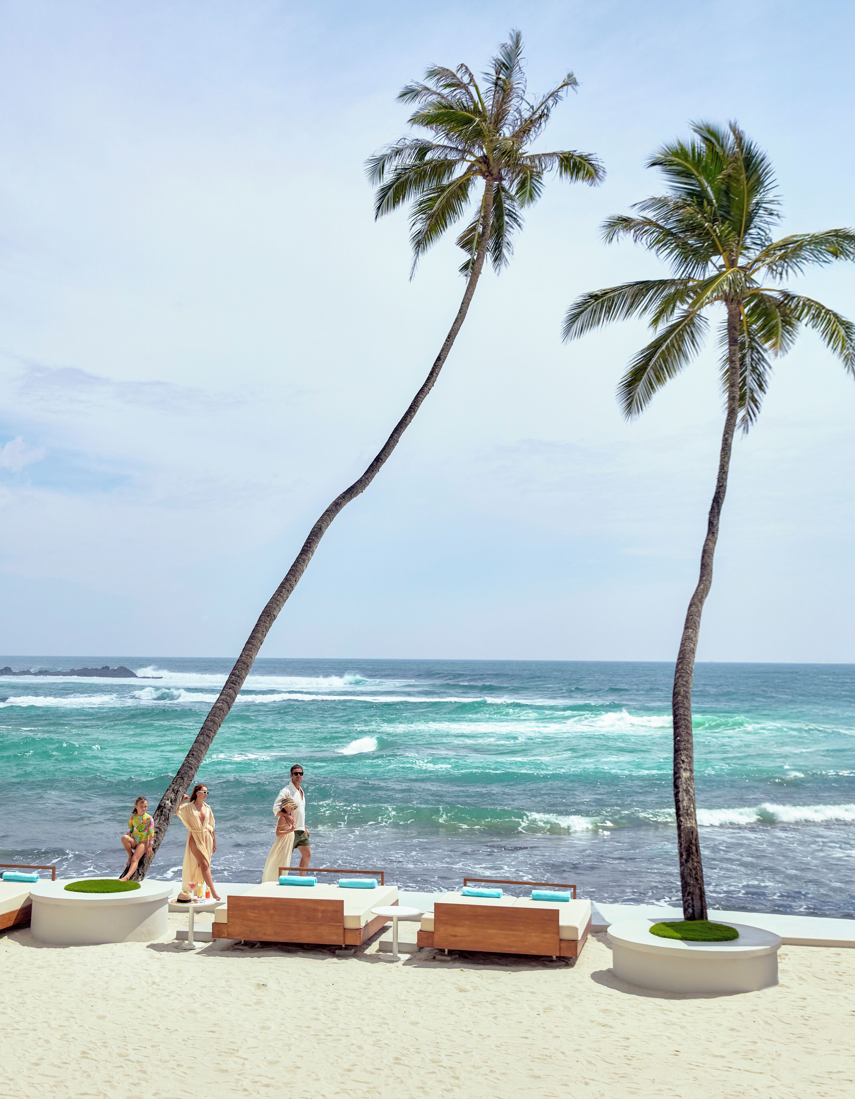 A beach with palm trees, ocean waves, and lounge chairs.
