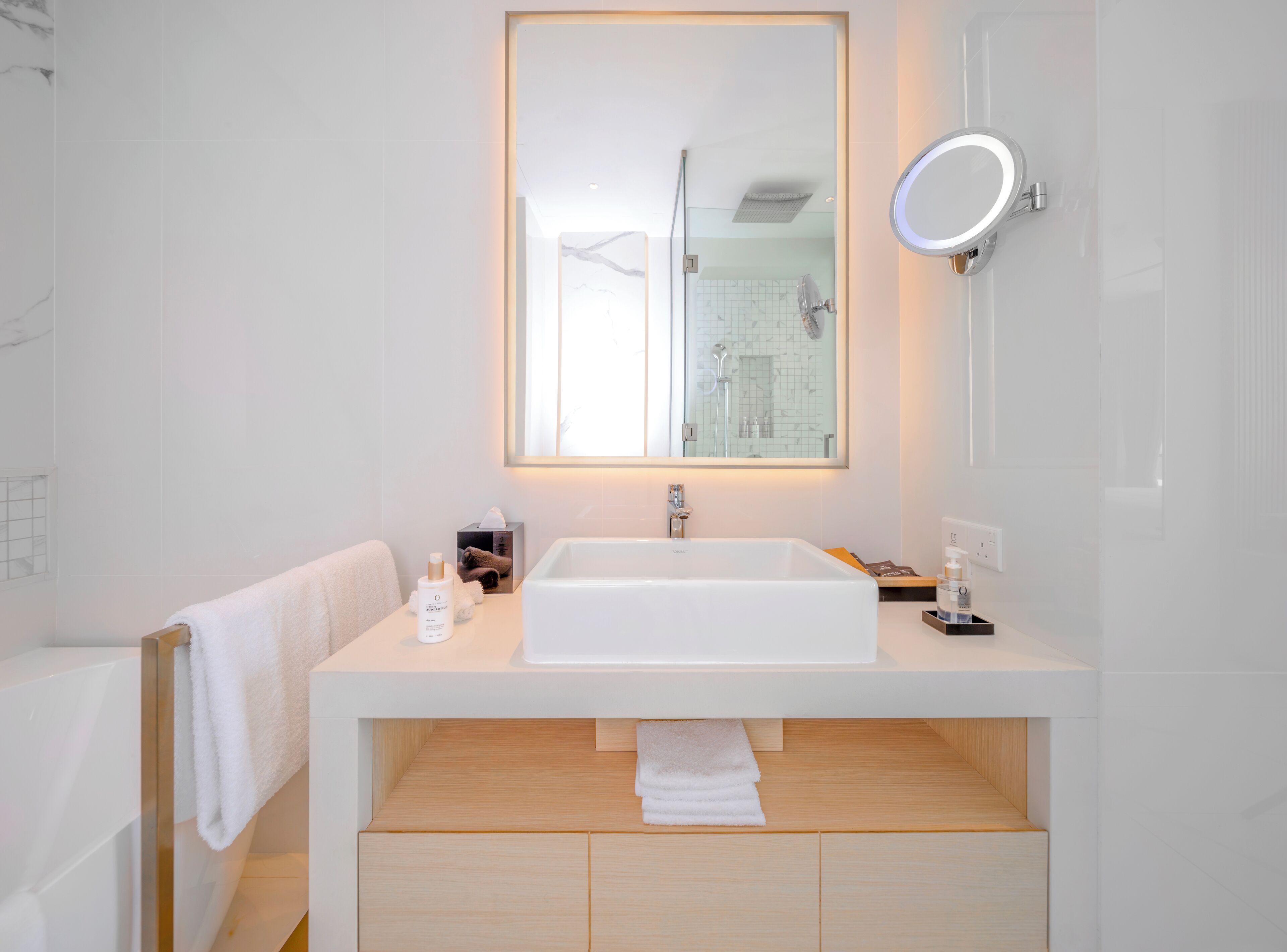 Une salle de bain moderne avec un lavabo blanc, un miroir et une douche visible à travers la porte en verre.