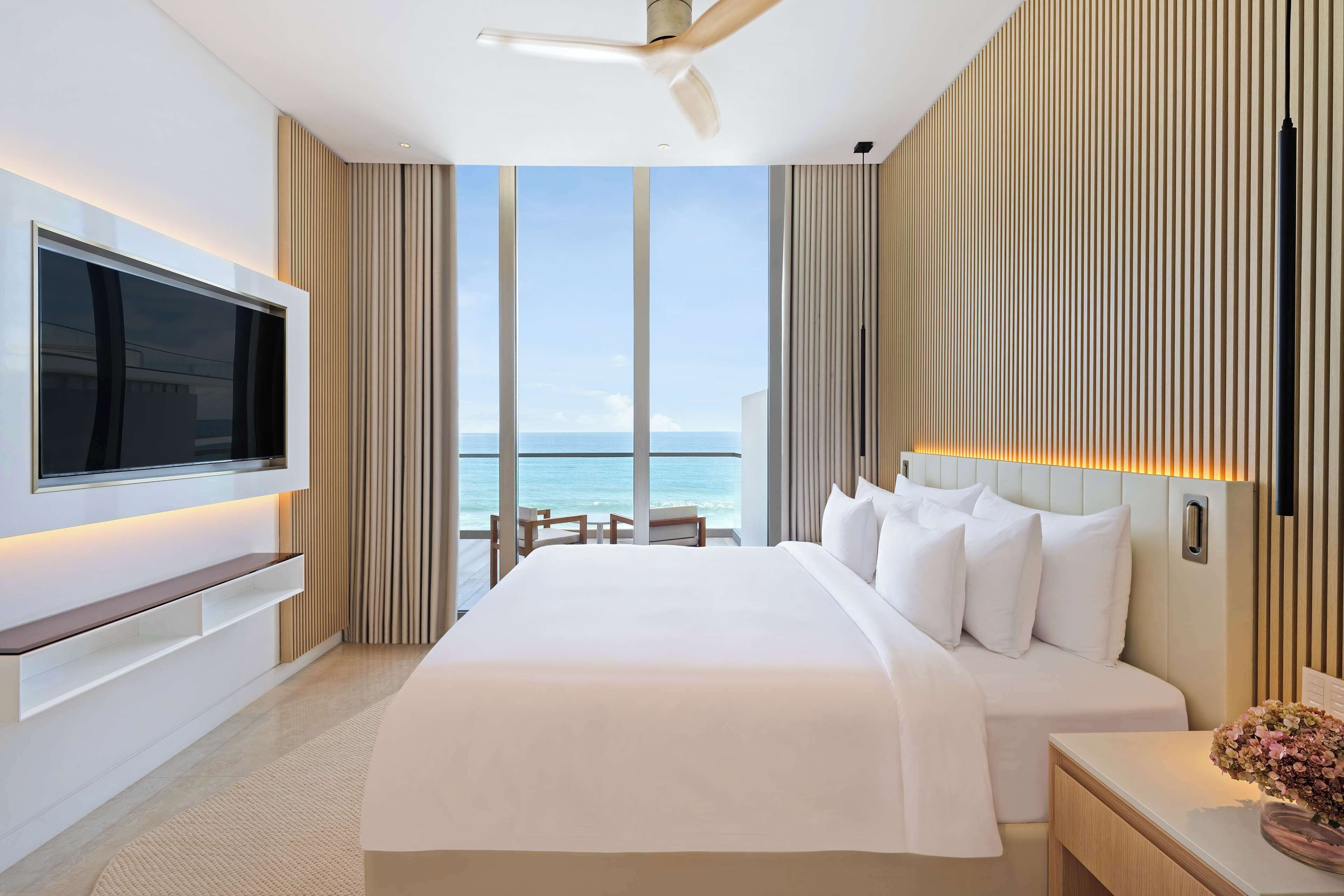 Ein modernes Hotelzimmer mit einem großen Bett, einem flachbildfernseher an der Wand, einem Deckenventilator und Blick auf den Ozean.
