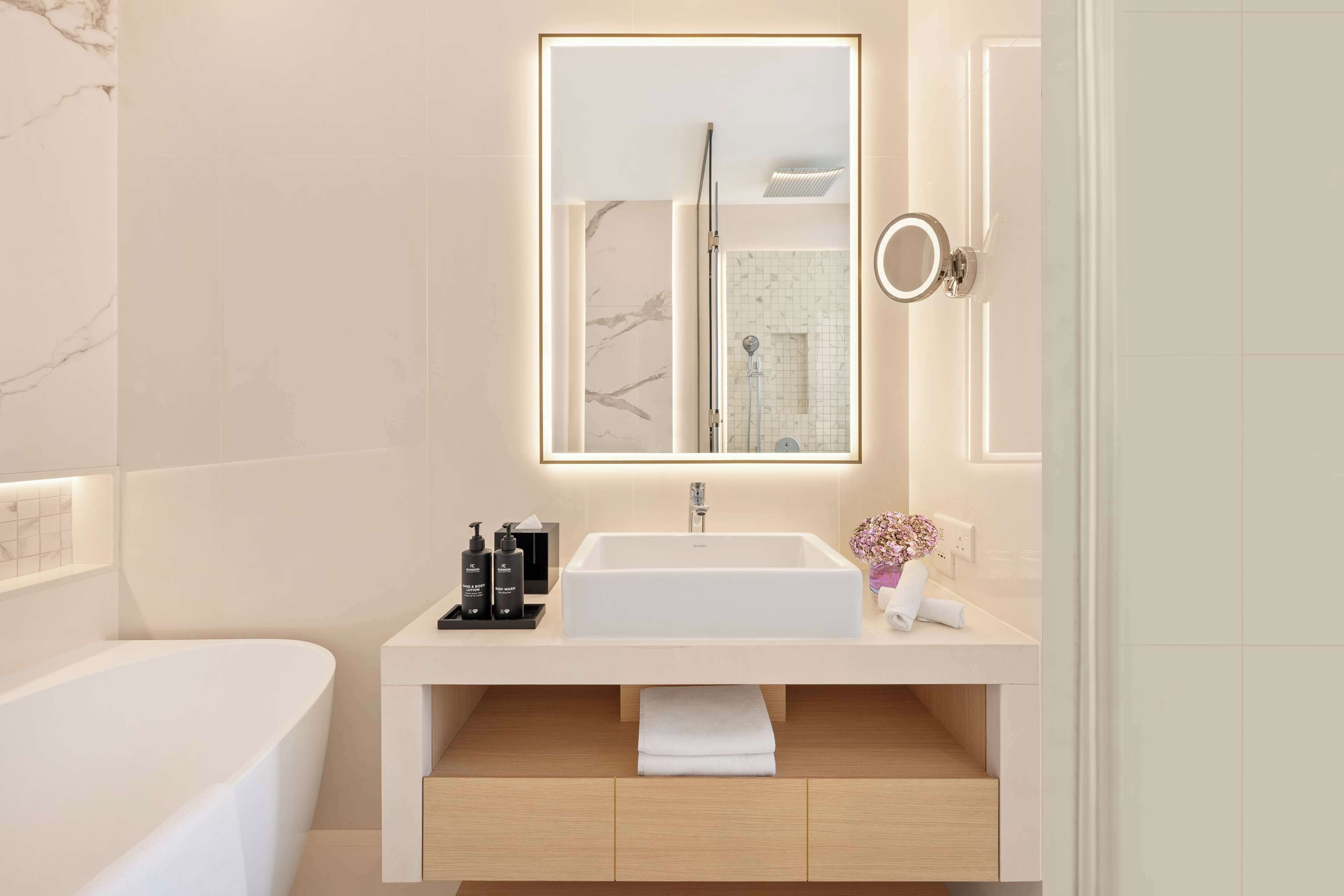 Un baño moderno con un lavamanos grande de color blanco, un espejo con iluminación integrada, un cabezal de ducha de mano y un inodoro.