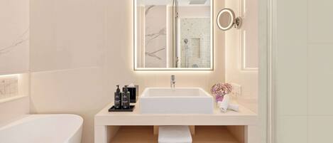 Un baño moderno con un lavamanos grande de color blanco, un espejo con iluminación integrada, un cabezal de ducha de mano y un inodoro.