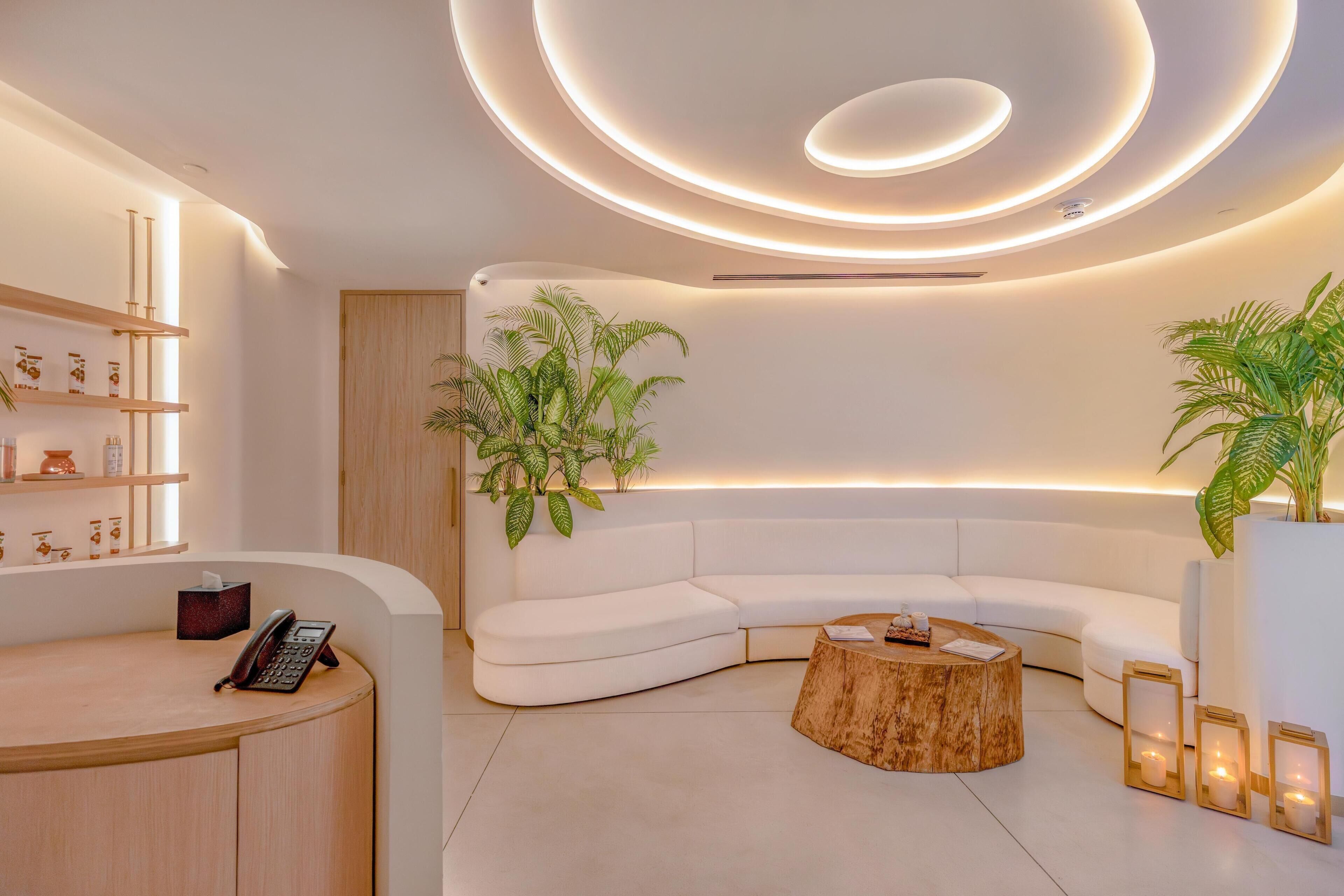 Ein moderner Empfangsbereich mit einer gebogenen weißen Couch, einem Holzbüro und stimmungsvoller Beleuchtung.