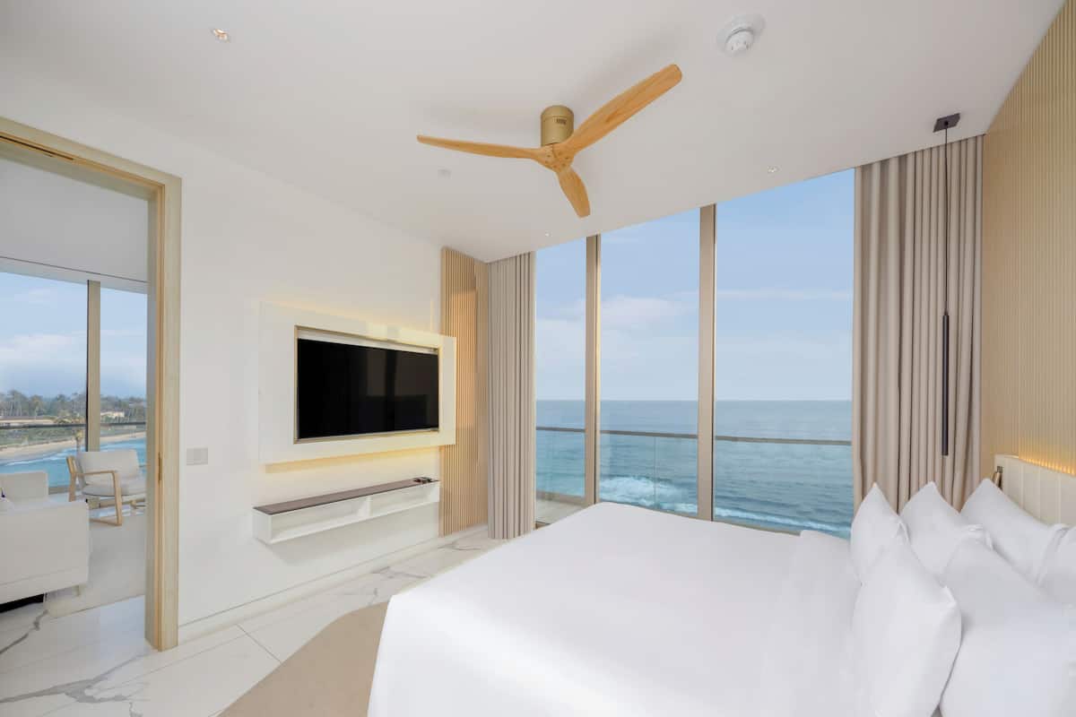 Une chambre d’hôtel moderne avec un grand lit, un téléviseur fixé au mur et une vue sur l’océan.