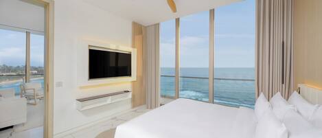 Habitación de hotel moderna con una cama grande, un televisor montado en la pared y vistas al océano.